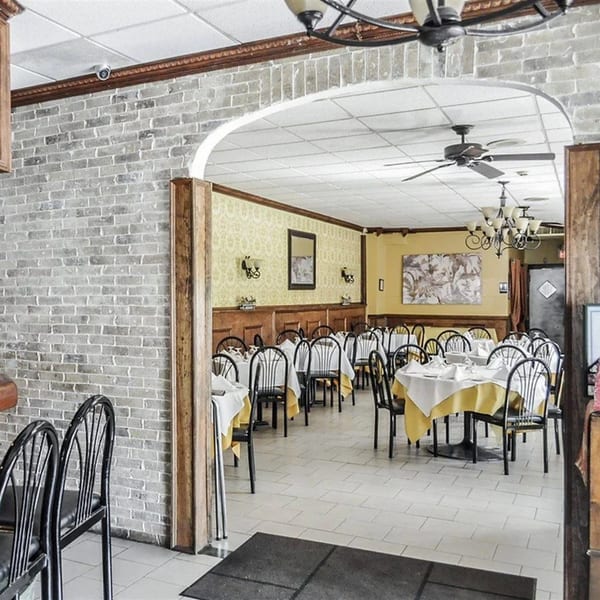 Dining room at Rini's Restaurant with set tables, yellow tablecloths, and brick archway.