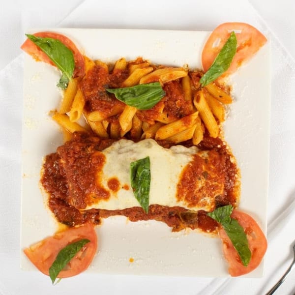 Baked ziti with melted cheese and penne pasta with marinara sauce, garnished with basil and tomato slices.