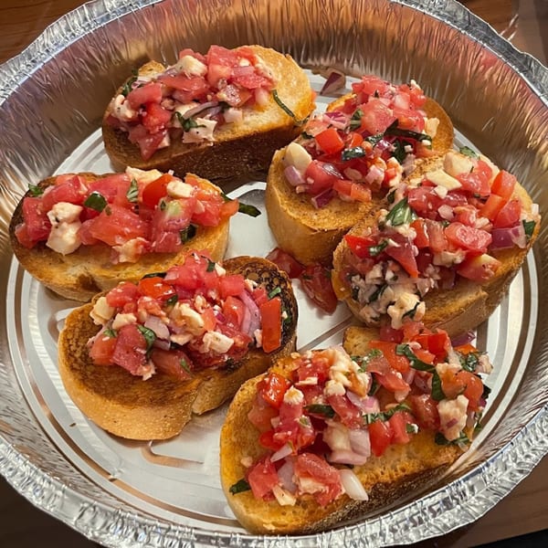 Six pieces of Rini's bruschetta with diced tomatoes, onions, and cheese in a foil container.