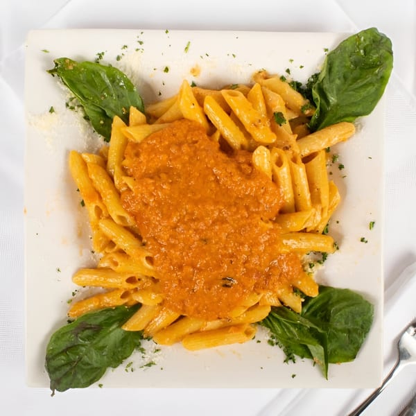 Penne pasta with orange sauce, garnished with fresh basil leaves and parsley on a white plate.