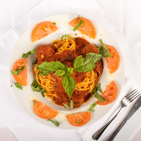 Spaghetti and meatballs with tomato sauce, fresh basil, and tomato slices on a white plate.
