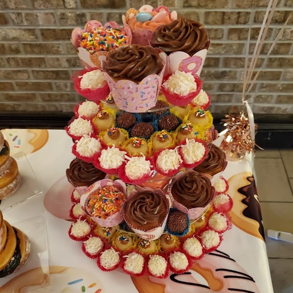 A tiered display of cupcakes, brigadeiros, and coconut truffles on a donut-patterned tablecloth.