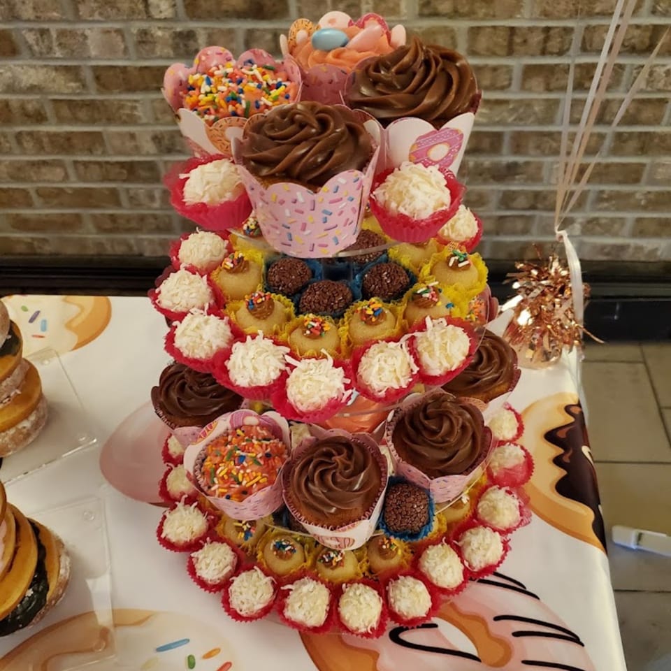 A tiered display of cupcakes, brigadeiros, and coconut truffles on a donut-patterned tablecloth.