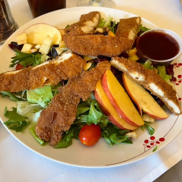 Crispy chicken tenders on a bed of mixed greens with apple slices, cherry tomato, and dipping sauce.