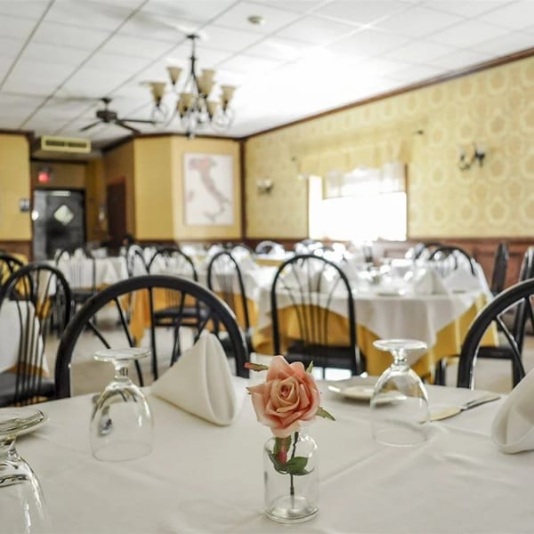 Dining room at Rini's Restaurant with set tables, white tablecloths, and a rose centerpiece.