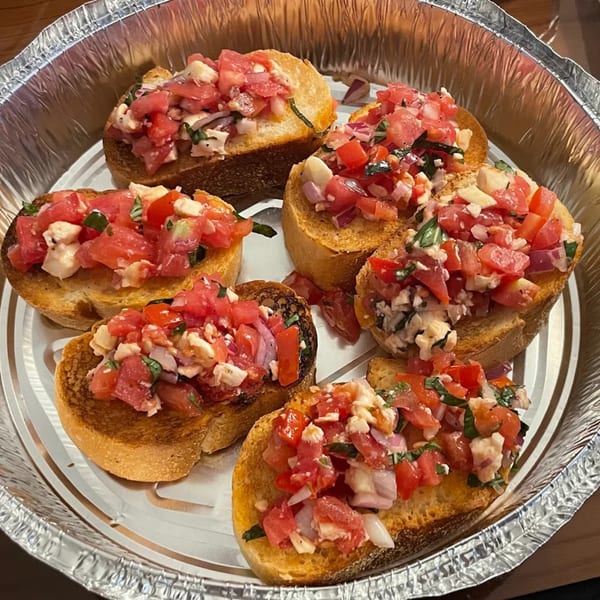 Rini's Restaurant & Wine Bar's bruschetta appetizer with diced tomatoes, onions, and cheese in a foil container.