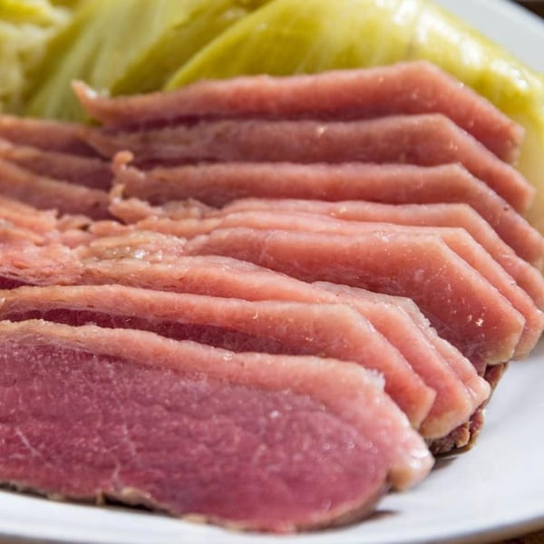 Thinly sliced corned beef with a side of green cabbage on a white plate.
