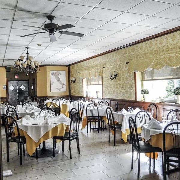 Dining room at Rini's Restaurant with set tables, a map of Italy, and patterned wallpaper.