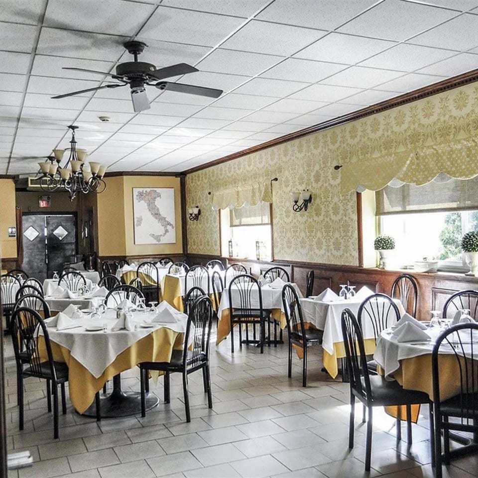 Dining room at Rini's Restaurant with set tables, a map of Italy, and patterned wallpaper.